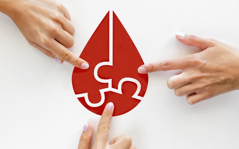 three hands touch a red shape that looks like a large drop of blood made up of three puzzle pieces