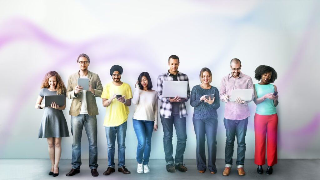 A diverse lineup of people are standing in a row as they use various digital devices.