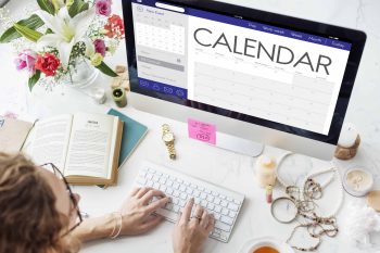 A woman sits in front of her laptop that displays an online calendar