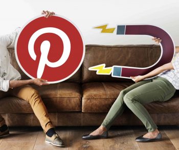 two people sitting on a couch, one holding a giant pinterest logo and the other holding a giant magnet that is attracting the pinterest logo