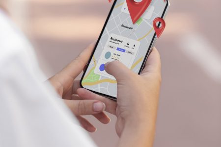 A view of a hand holding a smart phone with geographic red location markers overlaid on the image